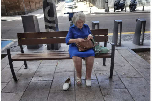 elderly woman sitting on public seat with one shoe off, in Madrid Spain