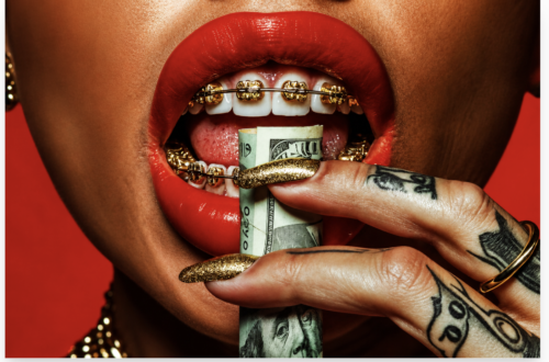 Extreme close-up of glossy red lips with gold braces biting a rolled US dollar bill, held by tattooed fingers with long gold glitter nails against a vivid red background, symbolising wealth, luxury and consumerism.