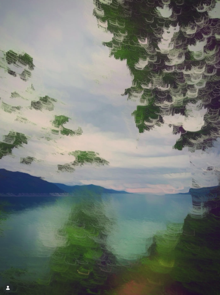 Abstract landscape photograph of a tranquil lake framed by trees, with impressionistic camera movement creating layered green foliage, soft pastel skies and shimmering reflections across the water.