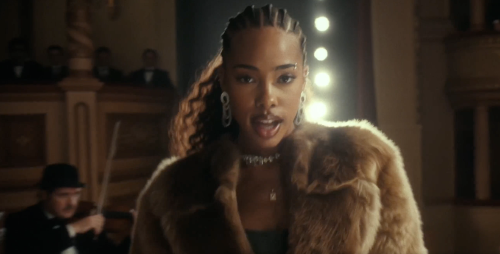 Higgsfield AI video generation example featuring a stylish woman in a fur coat performing on a theatre stage with dramatic lighting and an orchestra in the background, showcasing cinematic camera movement, realistic characters and high-production-value visuals.