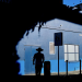 Silhouetted man in a wide-brimmed hat walking past a vivid blue building, framed by deep architectural shadows and strong sunlight.