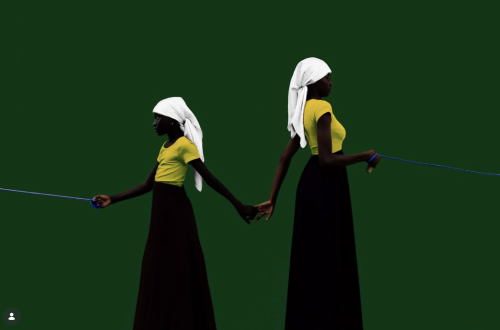 Two figures dressed in yellow tops, long black skirts and white headscarves stand against a deep green background, holding hands while each holds a blue skipping rope extending beyond the frame.Two figures dressed in yellow tops, long black skirts and white headscarves stand against a deep green background, holding hands while each holds a blue skipping rope extending beyond the frame.