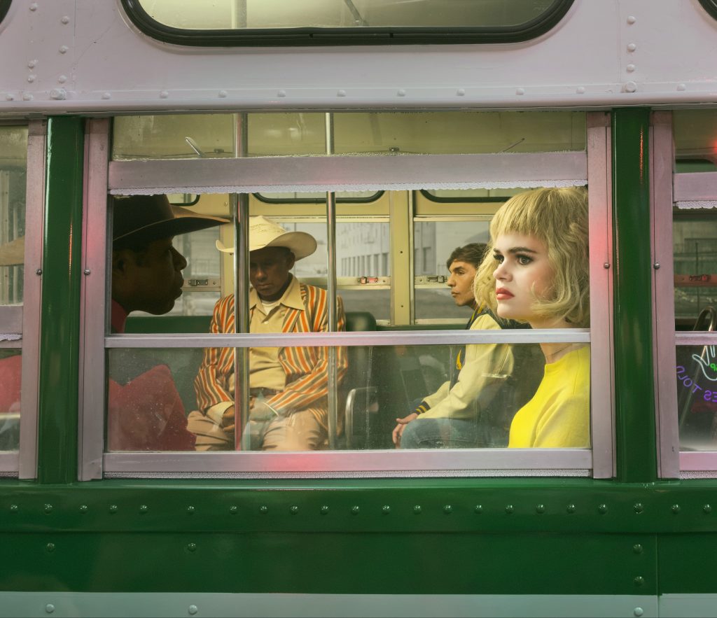 Alex Prager photograph of passengers in colourful retro clothing seen through the window of a bus.