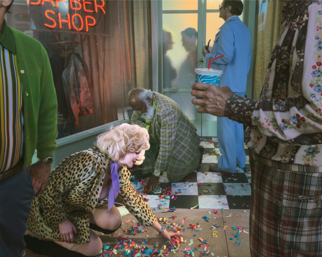 Alex Prager photograph of colourfully dressed figures gathering confetti inside a retro barbershop scene.