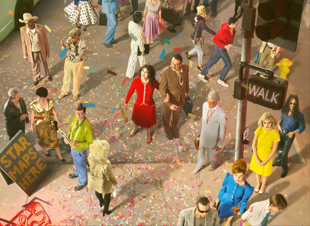 Alex Prager overhead photograph of pedestrians in vivid retro clothing moving through a street covered with colourful confetti.