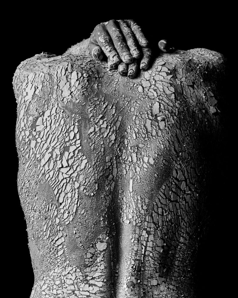 cracked back of model with hands covered in clay leaving textured black and white image